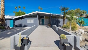 Una casa moderna con fachada de piedra, una puerta azul y un camino pavimentado que lleva a la entrada.