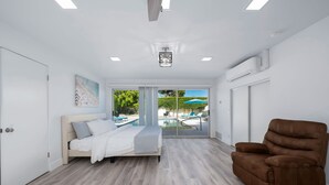 Un dormitorio moderno con una cama, un sillón marrón y vista a una piscina a través de puertas de cristal.