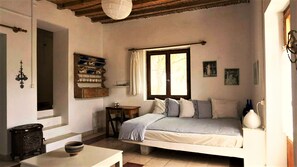 Une chambre confortable avec un lit, une petite table et une étagère où sont rangés de la vaisselle.