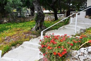 Un escalier en pierre avec une rampe métallique, entouré de verdure et de fleurs rouges.