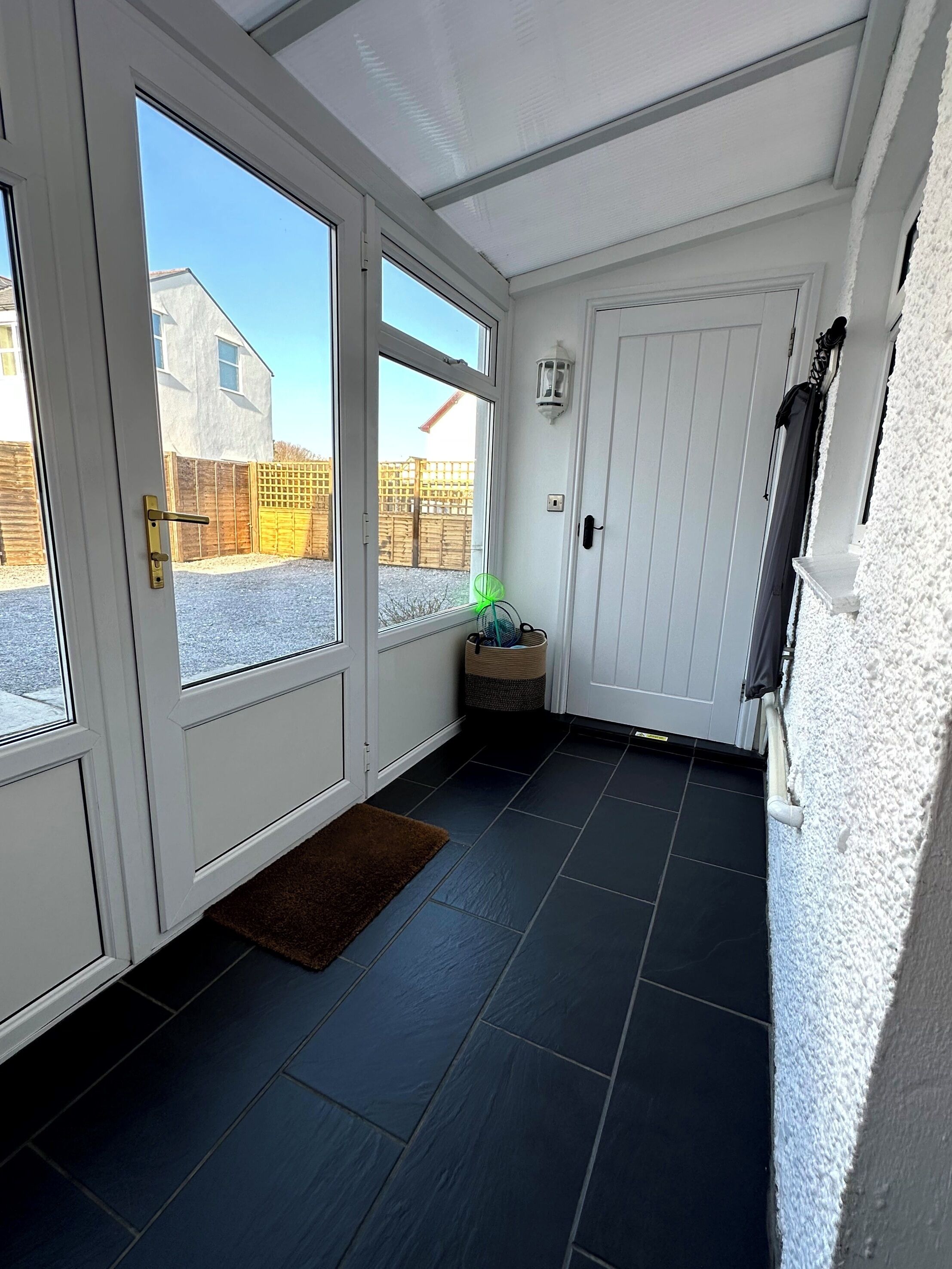 A clean, modern entryway with a glass door leading outside, a small basket, and a door with a light fixture.