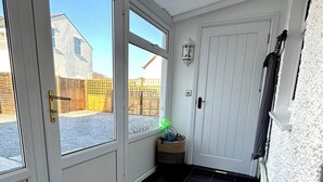 Un vestíbul net i modern amb una porta de vidre que dóna a l'exterior, una petita cistella i una porta amb una lluminària.