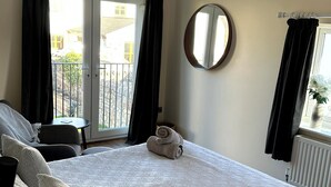 Un dormitori amb un llit gran, un mirall rodó i vistes al balcó exterior.