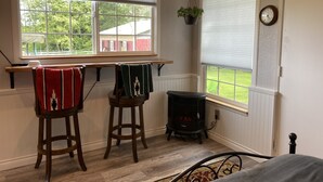 Een gezellige kamer met twee houten stoelen, een kleine verwarming en een raam met uitzicht op een rode schuur en groen.