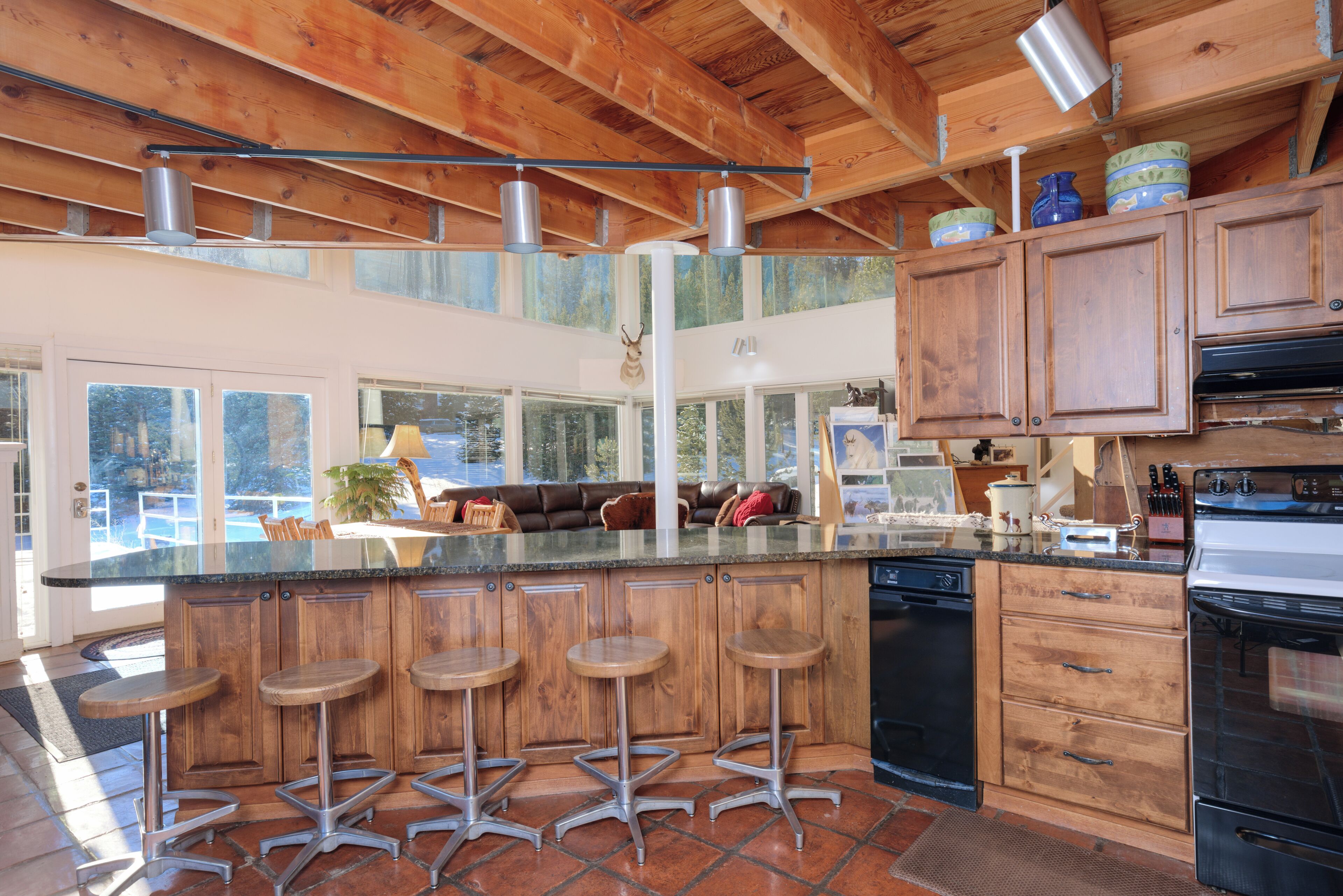A modern kitchen with wooden cabinets, a large island with stools, a dishwasher, and a stove.
