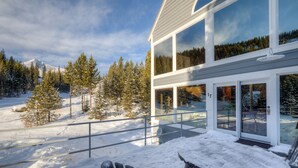 A modern building with large windows, a snow-covered deck, and a mountain backdrop. - Ski in/out home w/private hot tub, sauna, fireplace & great views - Low Dog Mountain Chalet (Big Sky)