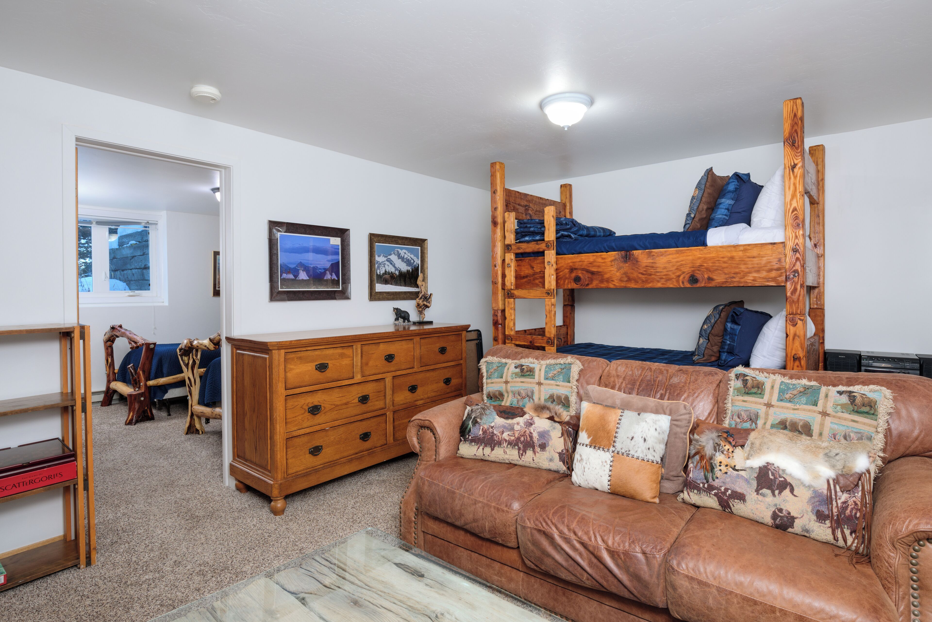 A cozy room with a bunk bed, a wooden dresser, a leather couch, and a mirror.