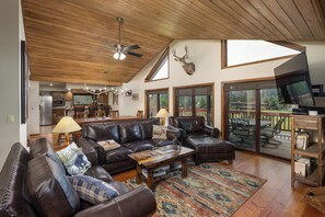 A spacious living room with leather furniture, a ceiling fan, and a mounted deer head. - Private Hot Tub | Golf Course | Nordic Skiing | Big Sky Awaits (Big Sky)