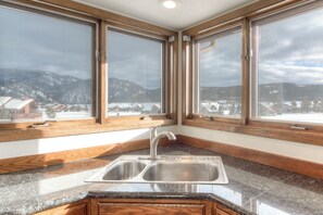 A kitchen with a double sink, wooden countertops, and large windows offering a view of a snowy landscape.