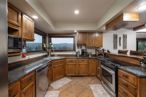 A kitchen with wooden cabinets, a stainless steel microwave, a coffee maker, and a large window offering a view of the outdoors.