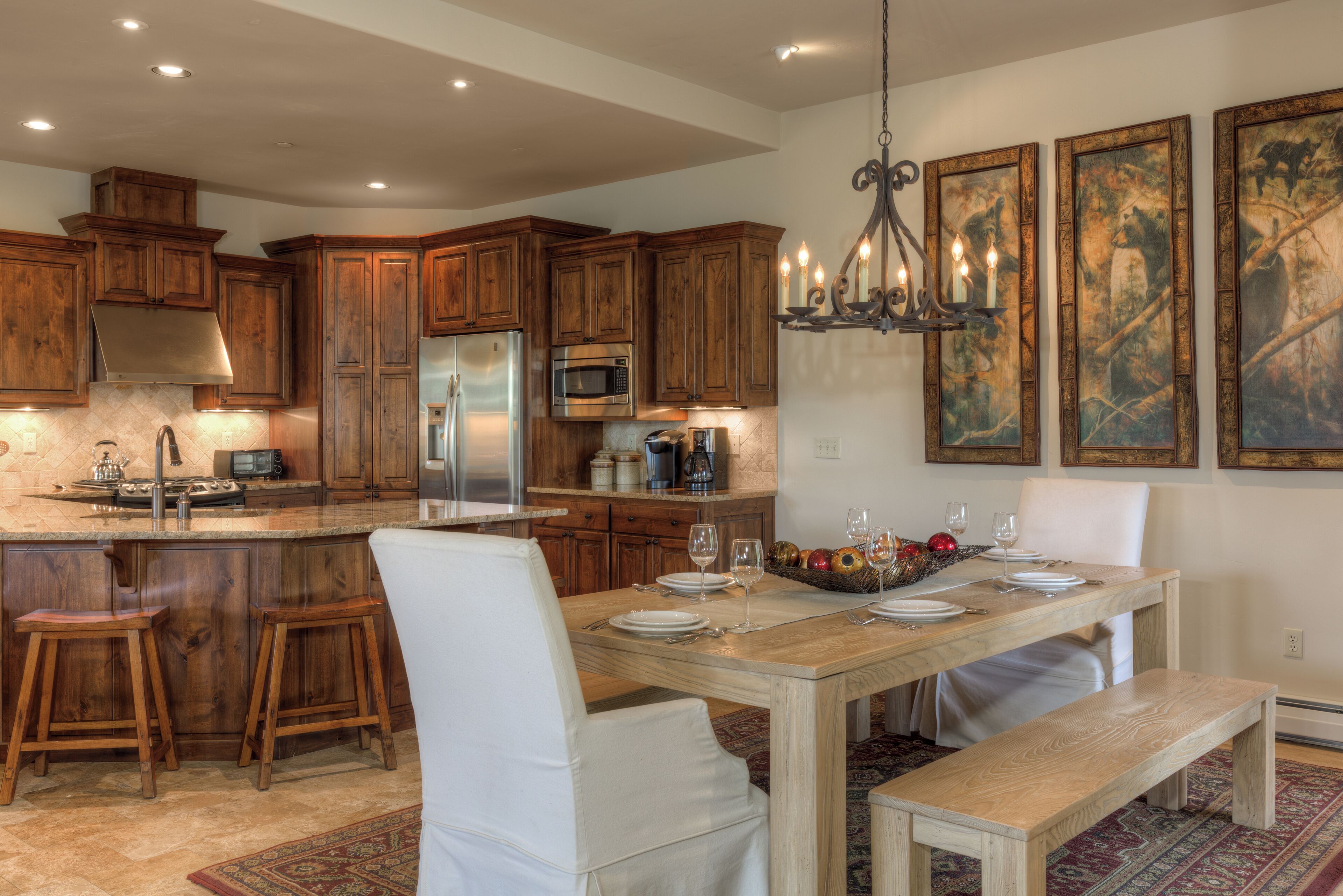 A spacious kitchen with wooden cabinets, a stainless steel refrigerator, and a dining area with a wooden table and white chairs.