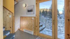 Een houten trap met uitzicht op een besneeuwd bos door een glazen deur.
