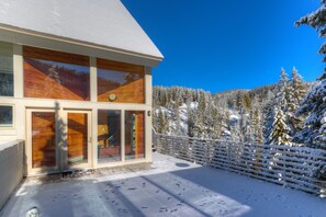 A modern house with large windows, a wooden facade, and a snow-covered landscape. - Ski-In/Ski-Out Home | Hot Tub, Sauna + Fireplace (Big Sky)