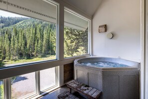 A room with a stone hot tub, large windows, and a view of a forested mountain.