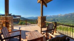 Une terrasse en bois avec une cheminée en pierre, des chaises en bois et une table offrant une vue sur un paysage montagneux.