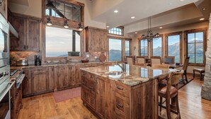 Une cuisine spacieuse avec des meubles en bois, un grand îlot central doté d’un évier et une vue sur les montagnes grâce à de grandes fenêtres.