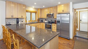 Une cuisine moderne avec des meubles en bois, un grand îlot central doté de tabourets, des appareils en acier inoxydable et un pare-feu en carrelage.