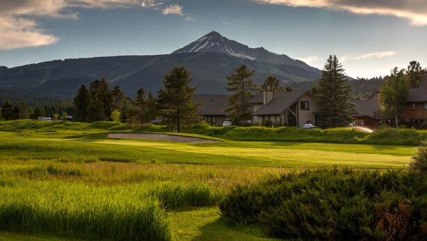 Un parcours de golf avec une montagne en arrière-plan, entouré d’immeubles résidentiels.