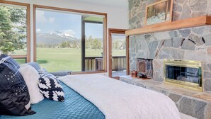 Een slaapkamer met een groot raam, een stenen openhaard en uitzicht op een berg.