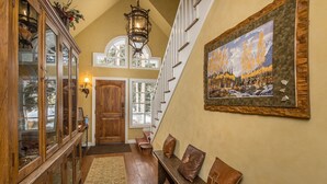 A wooden staircase with a bench, a glass cabinet, and a painting of a mountain landscape. - Secluded home close to Meadow Village w/private hot tub & library | Creekside Retreat (Big Sky)
