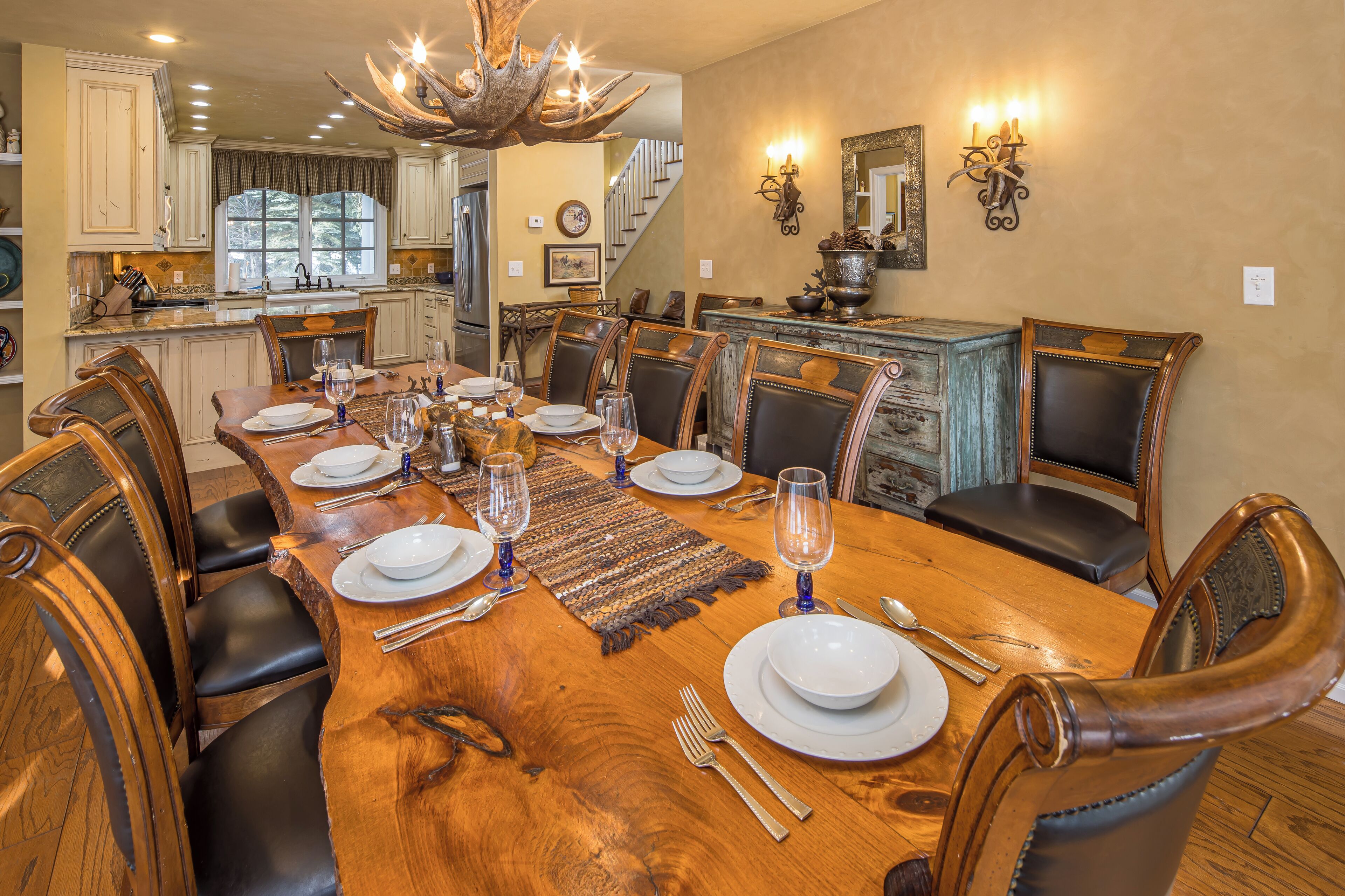 A dining room with a large wooden table set for six, surrounded by leather chairs.