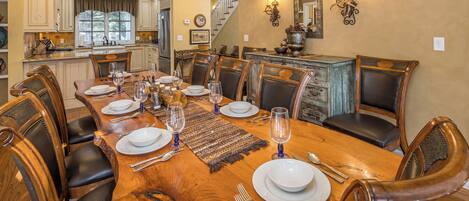 A dining room with a large wooden table set for six, surrounded by leather chairs.