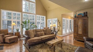 A spacious living room with a large brown sofa, two armchairs, a wooden coffee table, and a cabinet. - Secluded home close to Meadow Village w/private hot tub & library | Creekside Retreat (Big Sky)