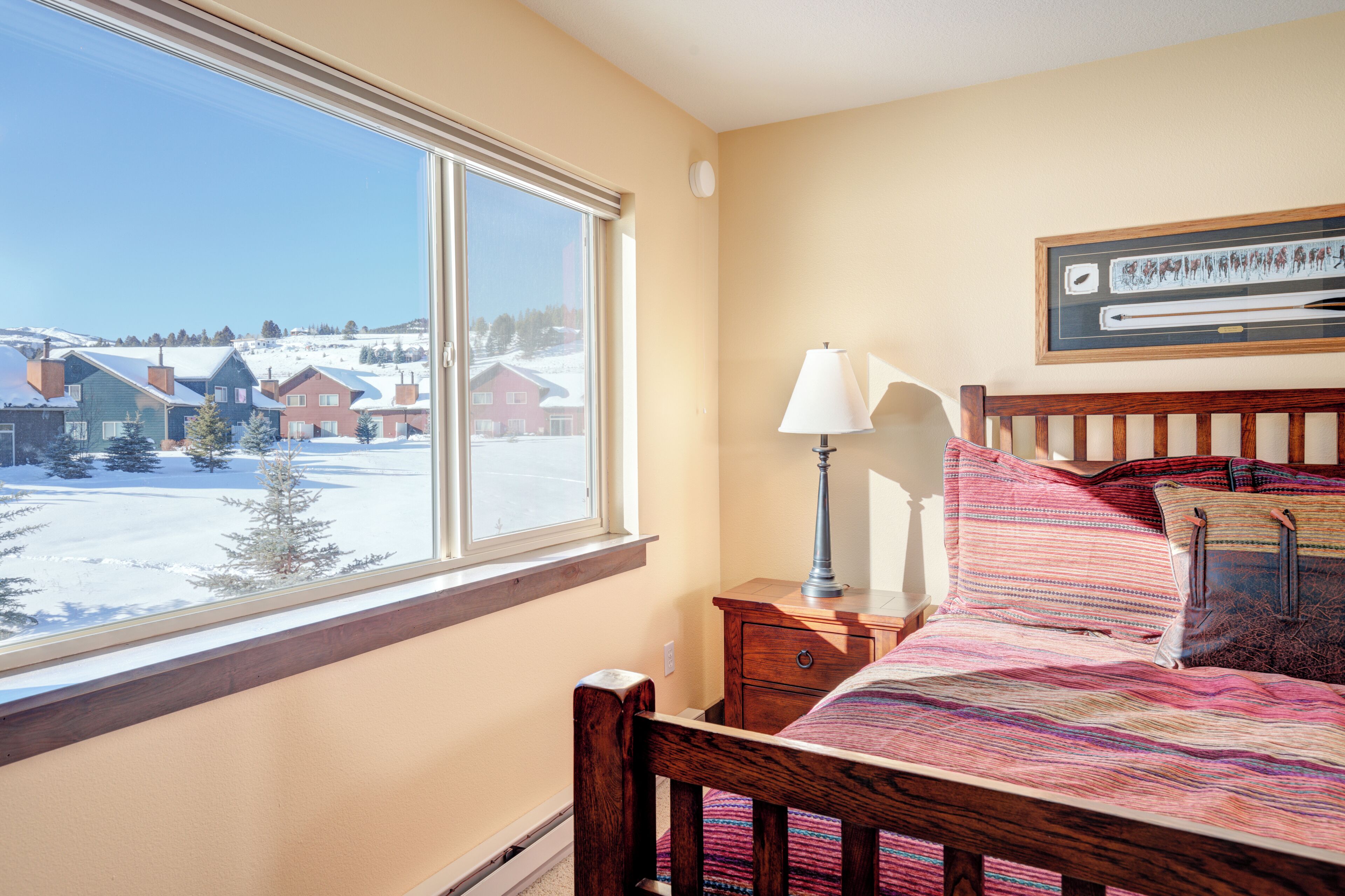 A bedroom with a large window, a wooden bed, a nightstand, and a lamp.