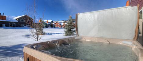 Un jacuzzi en un entorno nevado al aire libre, con un cielo azul despejado.