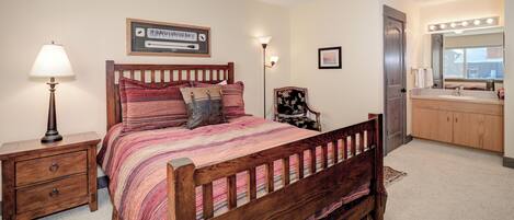 Un dormitorio con cama de madera, mesitas de noche, un tocador con espejo y una puerta.