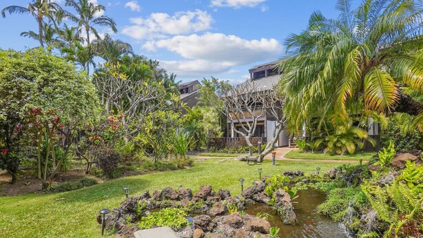 Un jardin tropical avec un étang, des palmiers et un bâtiment moderne.