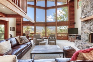 A spacious living area with a large window, a stone fireplace, leather sofas, and a flat-screen TV. - Home w/private hot tub, views, 2 master suites, close to Big Sky Resort - Chief Joseph Lodge (Big Sky)