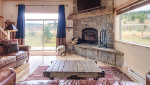 Un salon chaleureux avec une cheminée en pierre, un canapé en cuir et une grande fenêtre donnant sur une forêt.