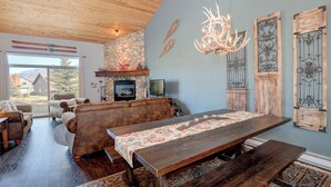 A spacious living room with a large wooden table, leather sofas, and a stone fireplace. - Beautiful home w/gorgeous views & fireplace, close to Big Sky Town Center - Firelight Cottage (Big Sky)
