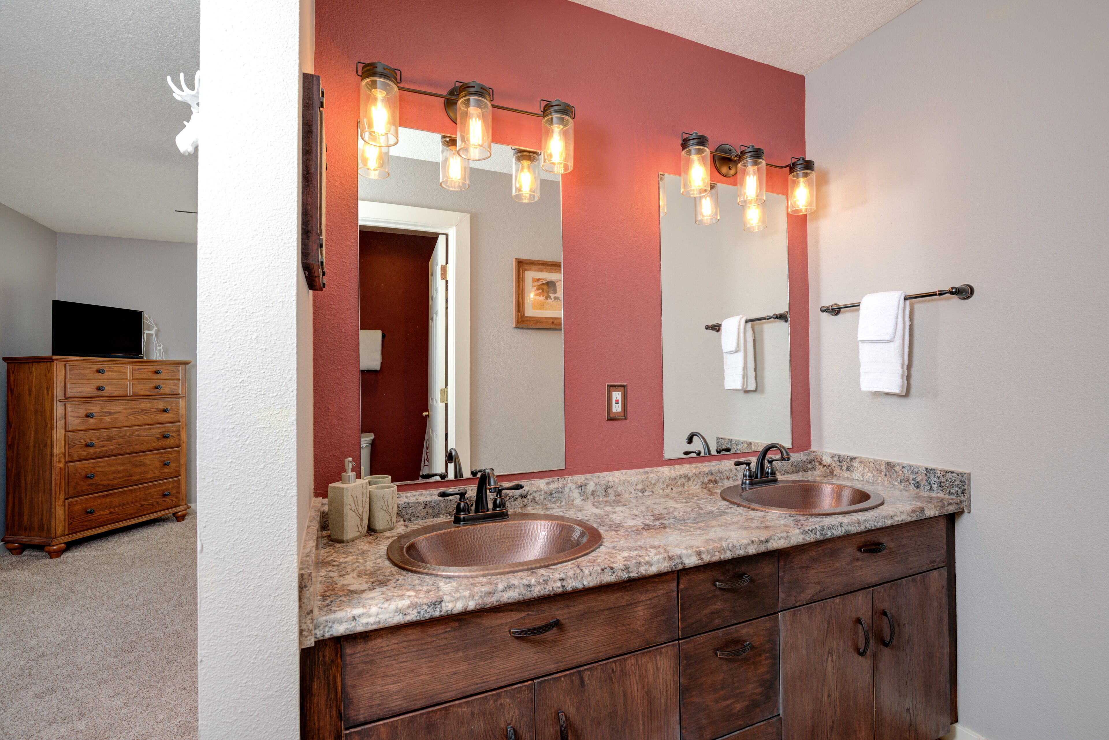 Une salle de bain dotée d’un meuble-lavabo à deux vasques, d’un meuble en bois et d’un grand miroir agrémenté de luminaires.