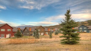 A residential area with houses, a grassy field, and a mountain in the background. - Beautiful home w/gorgeous views & fireplace, close to Big Sky Town Center - Firelight Cottage (Big Sky)