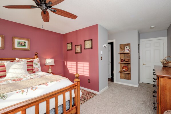 A bedroom with a wooden bed, a ceiling fan, and a door leading to another room.