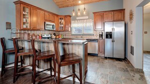 A kitchen with wooden cabinets, a stainless steel refrigerator, and a bar area with stools. - Beautiful home w/gorgeous views & fireplace, close to Big Sky Town Center - Firelight Cottage (Big Sky)