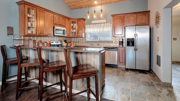 A kitchen with wooden cabinets, a stainless steel refrigerator, and a bar area with stools. - Beautiful home w/gorgeous views & fireplace, close to Big Sky Town Center - Firelight Cottage (Big Sky)