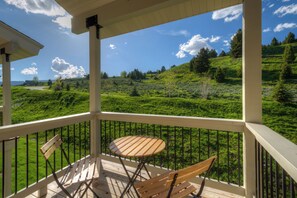 Un balcón con mesa y sillas de madera, con vista a un paisaje verde con árboles y colinas.