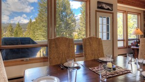 A dining area with a table set for four, large windows with a mountain view, patterned chairs, and a wooden ceiling. - Home in Big Sky Town Center w/fireplace & community pool/hot tub - Hidden Gem in the Trees (Big Sky)