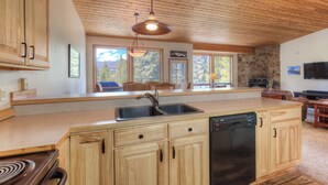 A kitchen with wooden cabinets, a dishwasher, and a stone accent wall. - Home in Big Sky Town Center w/fireplace & community pool/hot tub - Hidden Gem in the Trees (Big Sky)