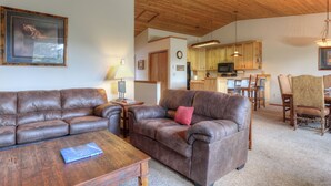 A living room with two brown leather sofas, a wooden coffee table, and a dining area with wooden chairs and a table. - Home in Big Sky Town Center w/fireplace & community pool/hot tub - Hidden Gem in the Trees (Big Sky)