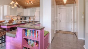 Una cocina moderna con techo de madera, armarios blancos y una isla central con una estantería rosa.