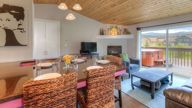 Un comedor con techo de madera, sillas de mimbre, una mesa con cubierta de vidrio y un televisor sobre un mueble.