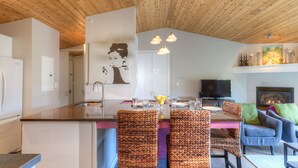 Una cocina moderna con una isla central, comedor con sillas de mimbre, un televisor de pantalla plana y una chimenea.