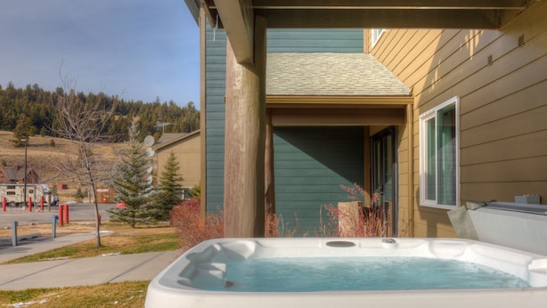 Un bain à remous à l’extérieur d’une maison, avec une terrasse en bois, un ciel dégagé et un paysage vallonné en arrière-plan.