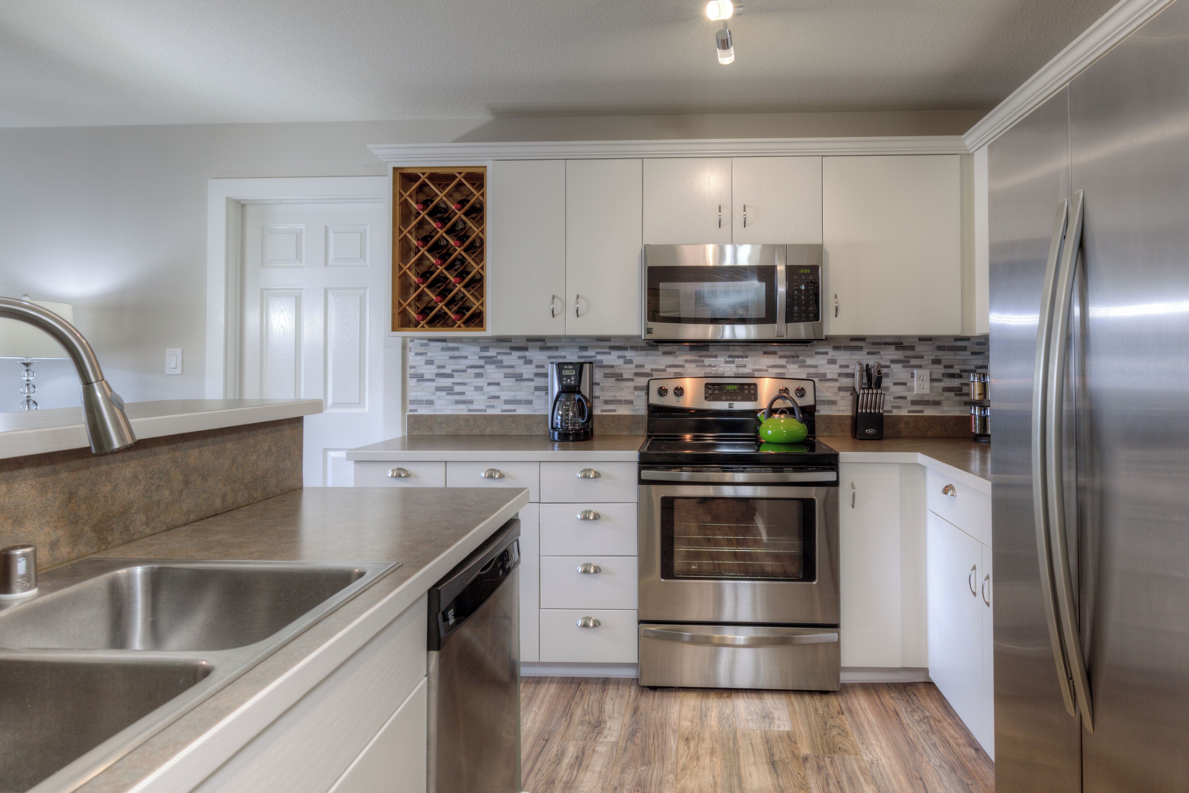 A modern kitchen with stainless steel appliances, white cabinetry, and a tiled backsplash.