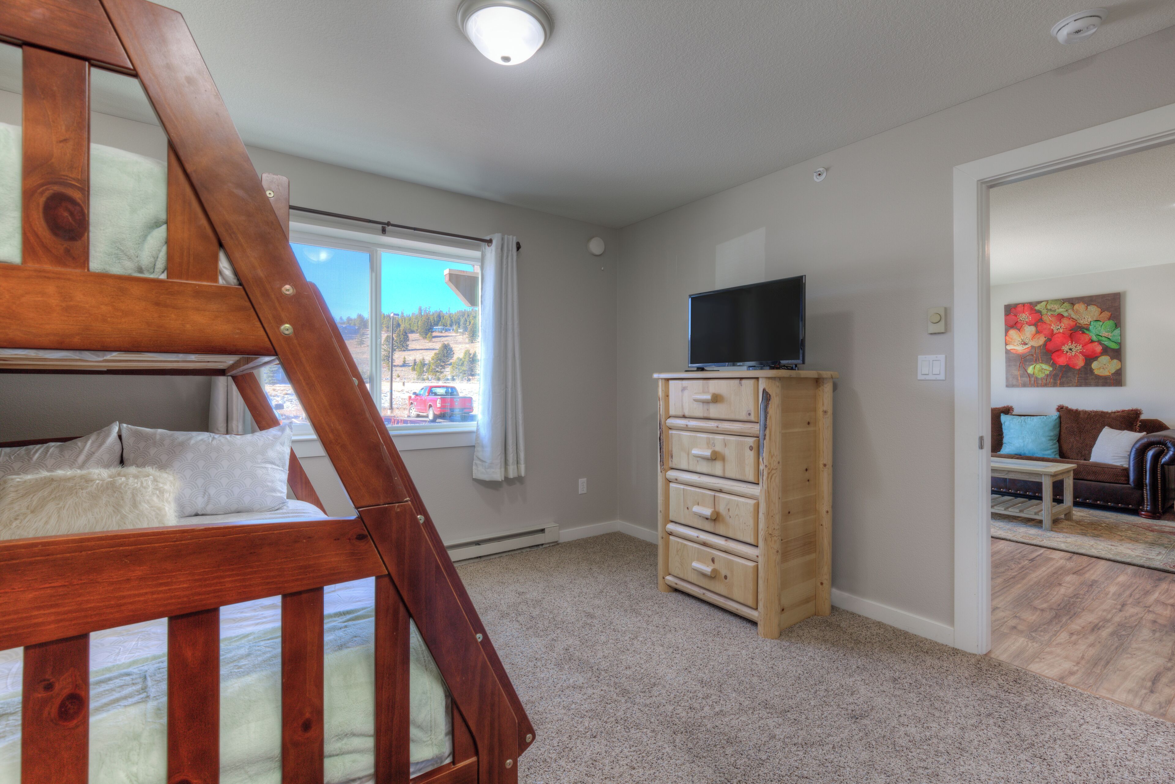 Une chambre avec un lit superposé, une commode en bois, un téléviseur et un tableau accroché au mur.
