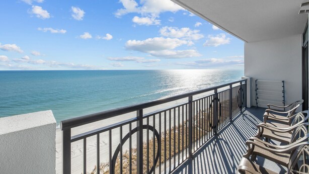 Ein Balkon mit Meerblick, einem Geländer und einer Reihe von Stühlen.